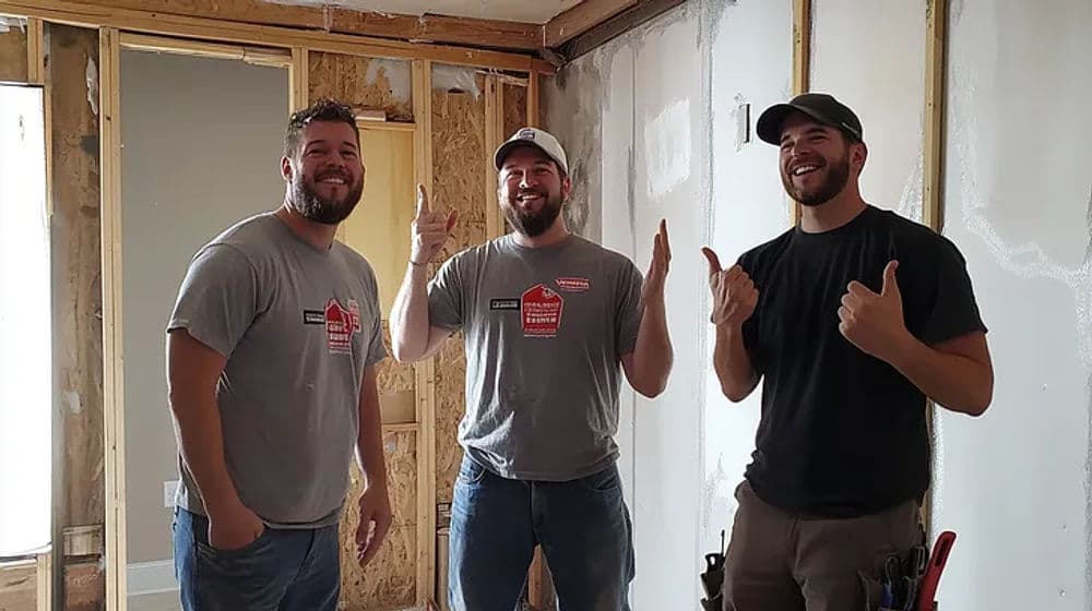 Three smiling construction workers in a partially renovated room, showcasing teamwork and progress.