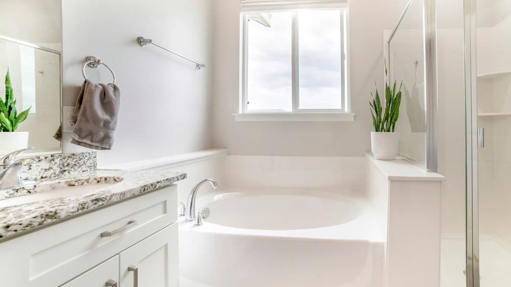Modern bathroom with a bathtub, stone countertop, large window, and potted plant.