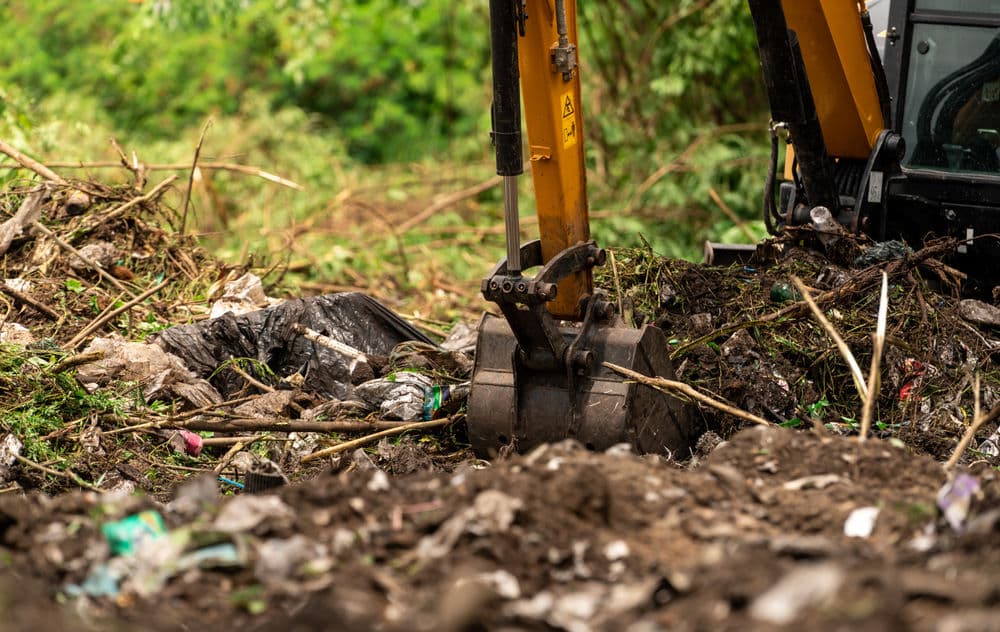 Excavator digging through debris and waste in a landfill site.