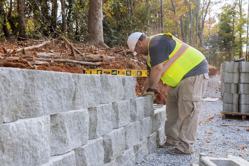 Worker in reflective safety vest constructing a stone wall with a spirit level outdoors.